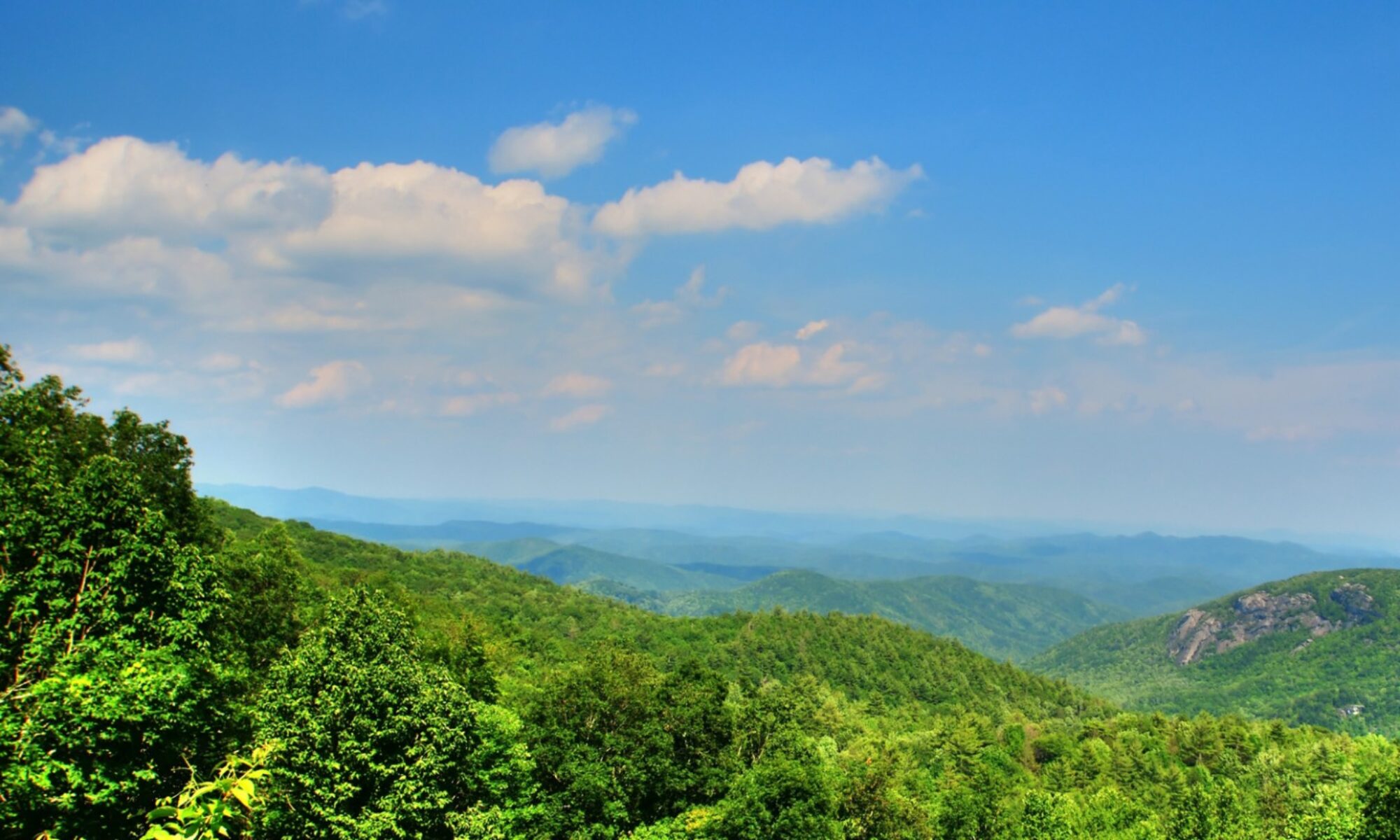 Photo showing green hills with blue sky and clouds.